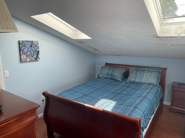bedroom with vaulted ceiling with skylight, a textured ceiling, and hardwood / wood-style flooring