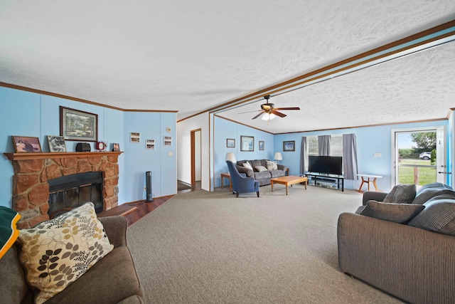 carpeted living room with a textured ceiling, a stone fireplace, ceiling fan, and ornamental molding