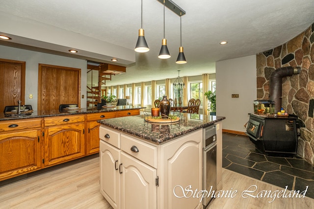 kitchen featuring a textured ceiling, decorative light fixtures, a center island, light hardwood / wood-style floors, and a wood stove