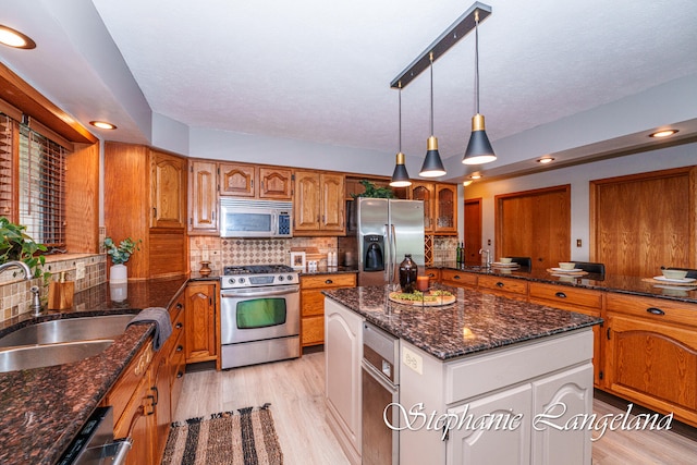 kitchen with sink, a center island, stainless steel appliances, light hardwood / wood-style flooring, and backsplash