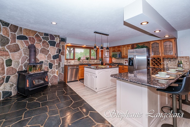 kitchen with a center island, backsplash, hanging light fixtures, appliances with stainless steel finishes, and light hardwood / wood-style floors