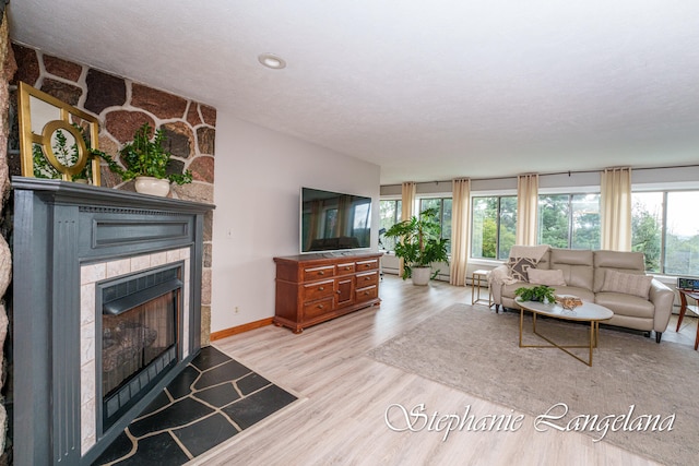 living room featuring a textured ceiling, light hardwood / wood-style floors, a stone fireplace, and a wealth of natural light