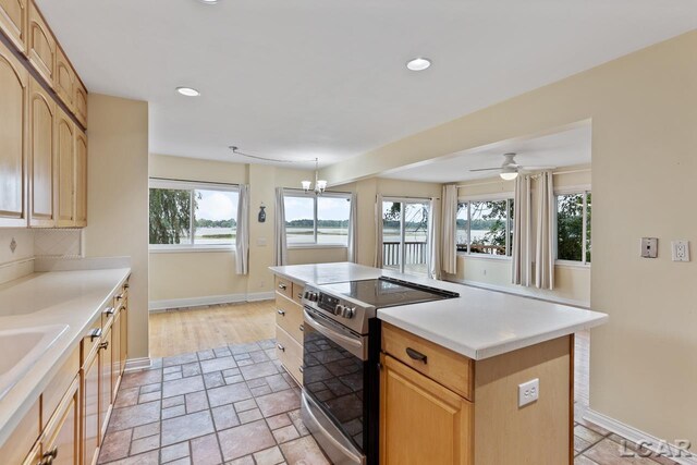 kitchen featuring tasteful backsplash, stainless steel range with electric stovetop, ceiling fan with notable chandelier, light brown cabinets, and a center island