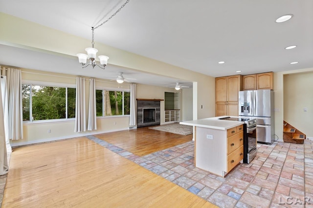 kitchen with light brown cabinets, ceiling fan with notable chandelier, appliances with stainless steel finishes, decorative light fixtures, and a kitchen island