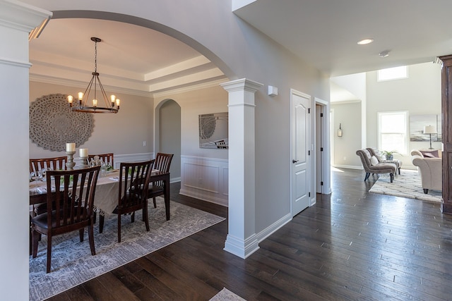 dining space featuring a notable chandelier, ornate columns, dark wood-type flooring, and a tray ceiling