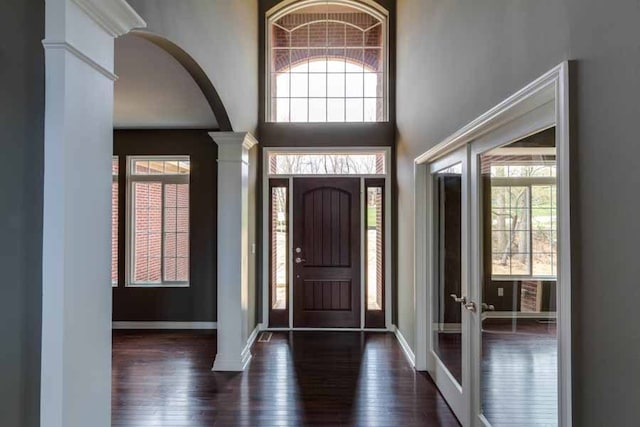 entryway with dark hardwood / wood-style floors, a healthy amount of sunlight, ornate columns, and a high ceiling