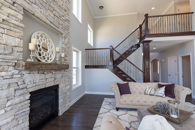 living room with dark wood-type flooring, ornamental molding, a fireplace, a towering ceiling, and decorative columns