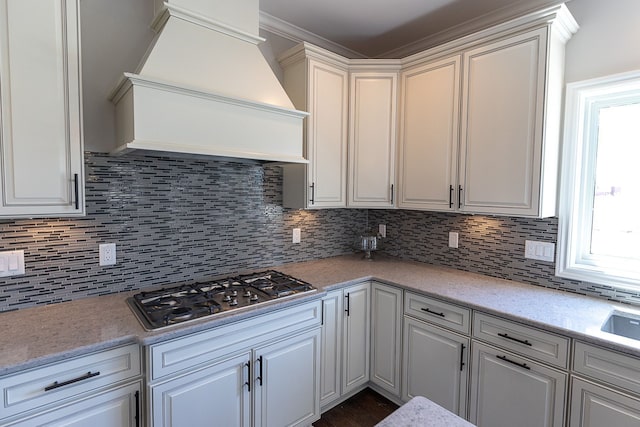 kitchen with backsplash, crown molding, custom range hood, and stainless steel gas cooktop