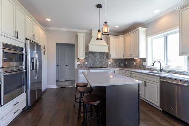 kitchen with dark wood-type flooring, crown molding, sink, appliances with stainless steel finishes, and a kitchen island