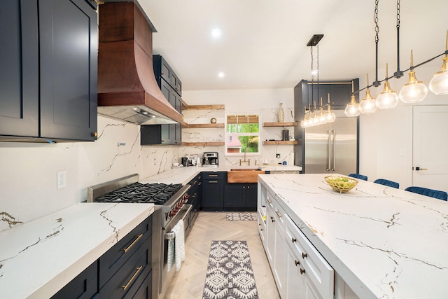 kitchen with premium range hood, light stone counters, high end appliances, white cabinets, and hanging light fixtures