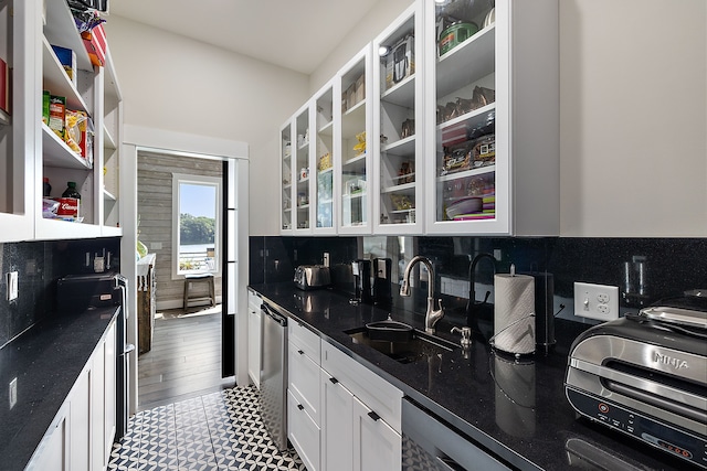 kitchen with white cabinets, sink, stainless steel dishwasher, dark stone countertops, and tasteful backsplash