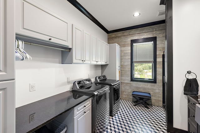 washroom with cabinets, wooden walls, and washing machine and clothes dryer