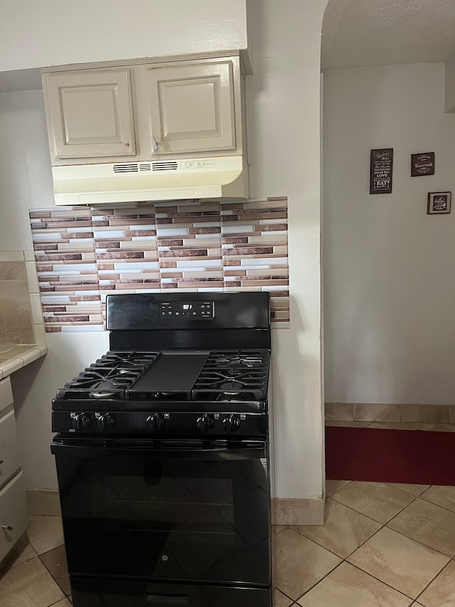 kitchen with light tile patterned flooring, black gas range, backsplash, and range hood