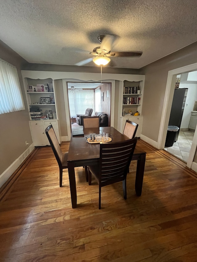 dining room with wood-type flooring, a textured ceiling, built in features, and ceiling fan