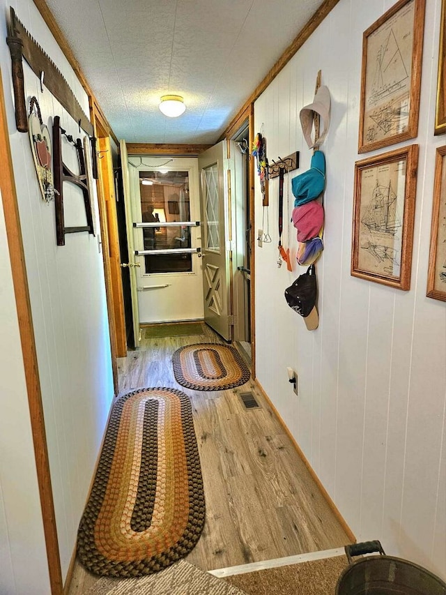 hall with a textured ceiling, wooden walls, and light hardwood / wood-style flooring