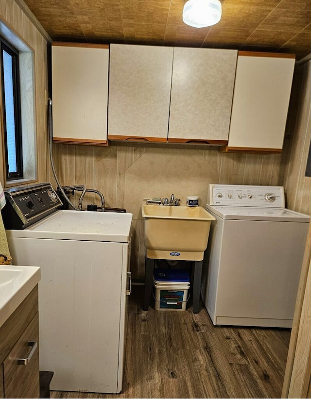 laundry area with cabinets, sink, washing machine and clothes dryer, dark hardwood / wood-style floors, and wood walls