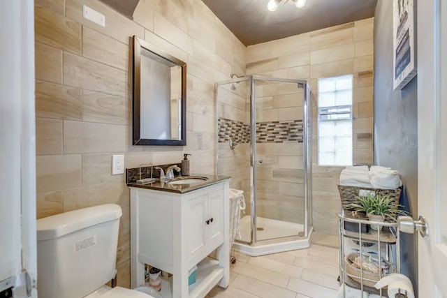 bathroom with vanity, toilet, a shower with door, and tile walls