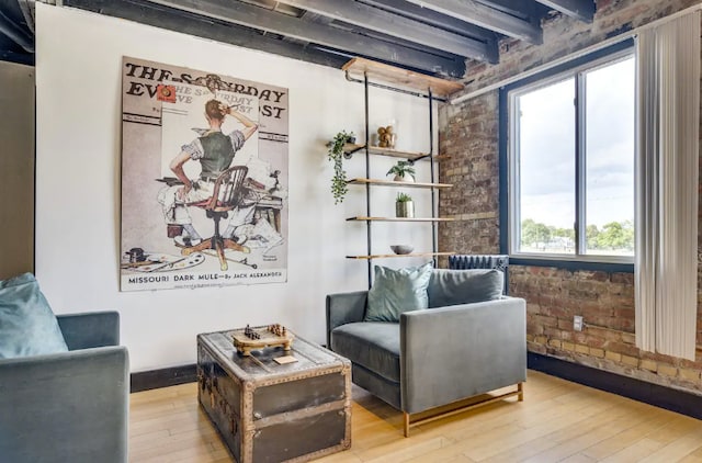 living area featuring beam ceiling, light hardwood / wood-style floors, and brick wall