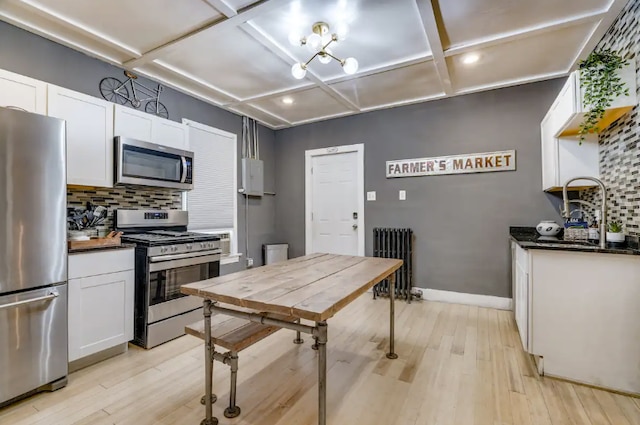 kitchen with decorative backsplash, appliances with stainless steel finishes, light wood-type flooring, radiator, and white cabinets