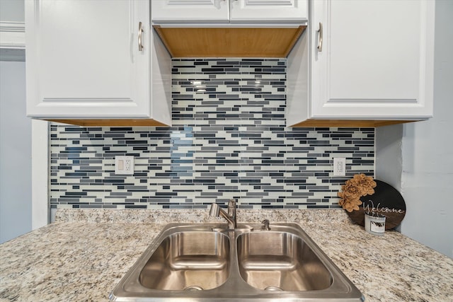 kitchen featuring light stone countertops, backsplash, white cabinetry, and sink