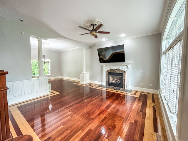 unfurnished living room with hardwood / wood-style flooring, decorative columns, crown molding, and a tiled fireplace