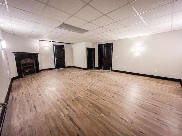 basement featuring a premium fireplace, a drop ceiling, and light hardwood / wood-style floors