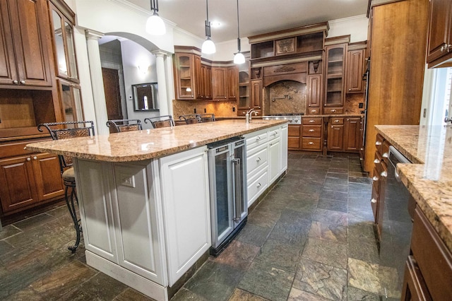 kitchen featuring wine cooler, decorative columns, pendant lighting, a breakfast bar, and a center island with sink