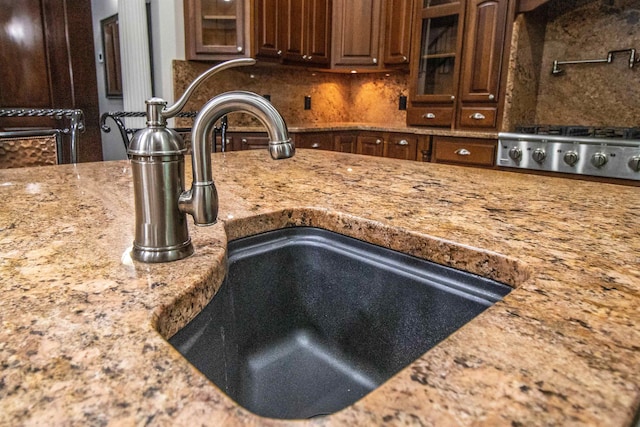 kitchen with stainless steel gas stovetop, decorative backsplash, sink, and stone counters