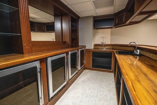 kitchen with wood counters, a drop ceiling, beverage cooler, and sink