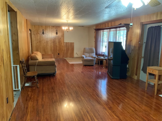 living room with hardwood / wood-style floors, ceiling fan with notable chandelier, a textured ceiling, and wood walls