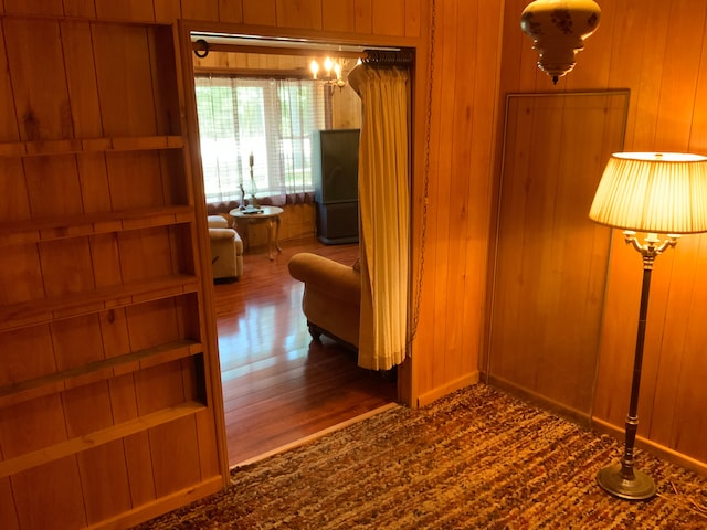 corridor featuring wooden walls, an inviting chandelier, and dark wood-type flooring