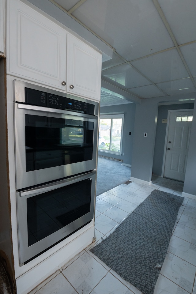 kitchen with white cabinets, stainless steel double oven, and a paneled ceiling