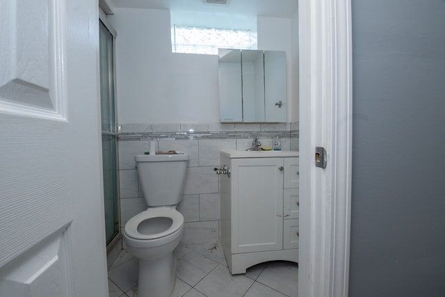 bathroom with vanity, a shower with door, tile walls, tile patterned flooring, and toilet