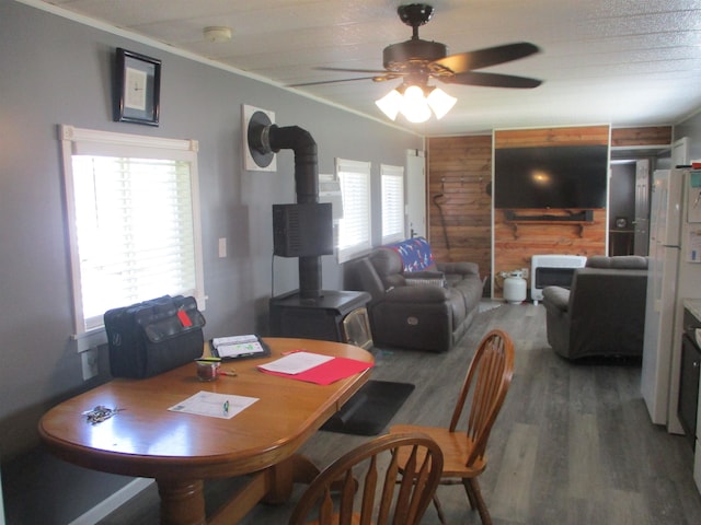 dining area featuring a wood stove, ceiling fan, wood-type flooring, and wood walls