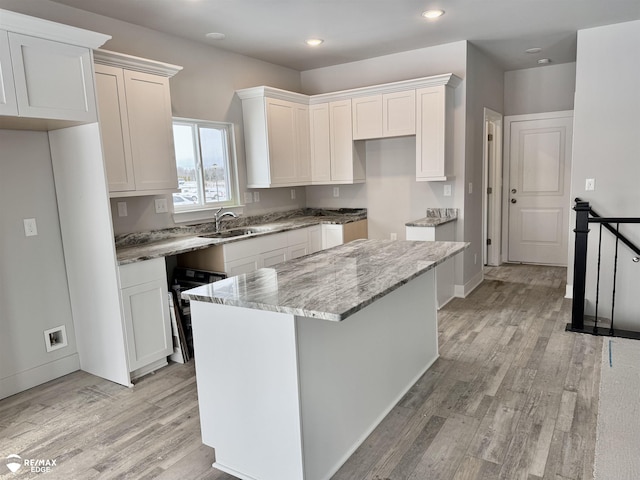 kitchen with sink, white cabinetry, light wood-type flooring, a kitchen island, and light stone countertops