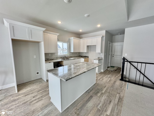 kitchen with sink, light hardwood / wood-style flooring, a kitchen island, light stone countertops, and white cabinets