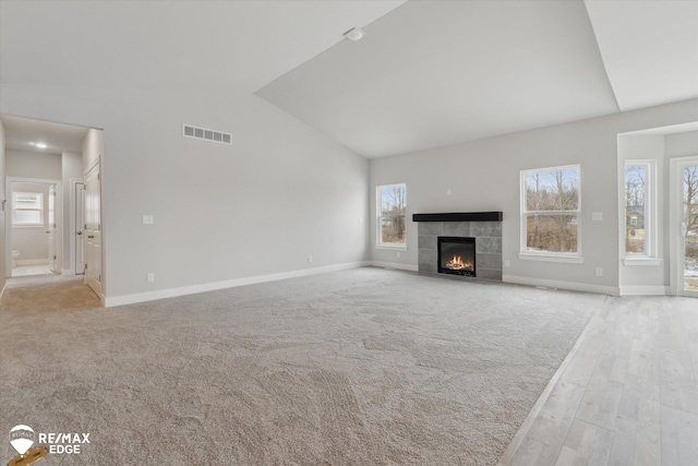 unfurnished living room featuring a fireplace, visible vents, light wood-style flooring, vaulted ceiling, and baseboards