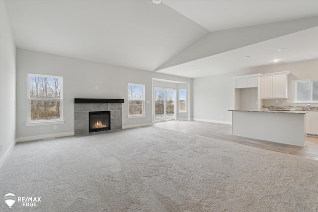 unfurnished living room featuring high vaulted ceiling, baseboards, a tiled fireplace, and light colored carpet