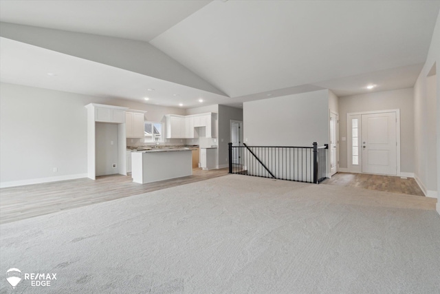 unfurnished living room with high vaulted ceiling, light wood-style flooring, recessed lighting, light carpet, and baseboards