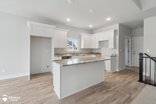 kitchen featuring light stone counters, white cabinetry, a kitchen island, and light wood-style flooring