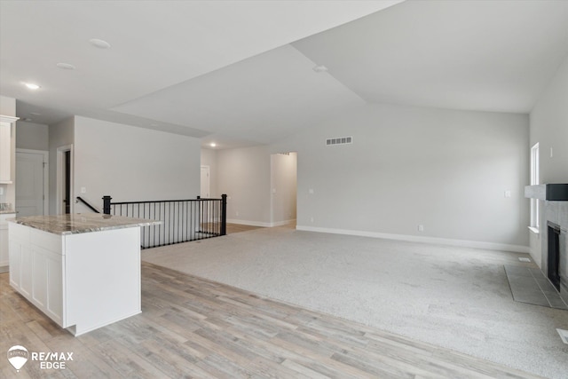 interior space with a fireplace, visible vents, light wood-style floors, white cabinets, and vaulted ceiling