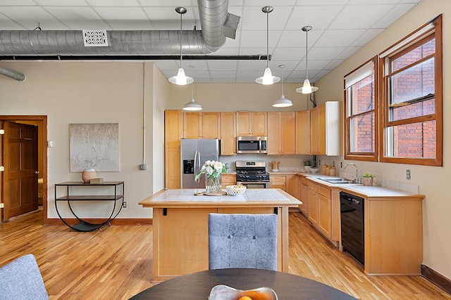 kitchen with tile counters, sink, hanging light fixtures, appliances with stainless steel finishes, and light wood-type flooring