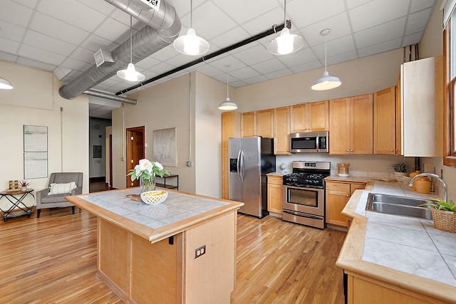 kitchen featuring pendant lighting, tile countertops, sink, light hardwood / wood-style flooring, and appliances with stainless steel finishes