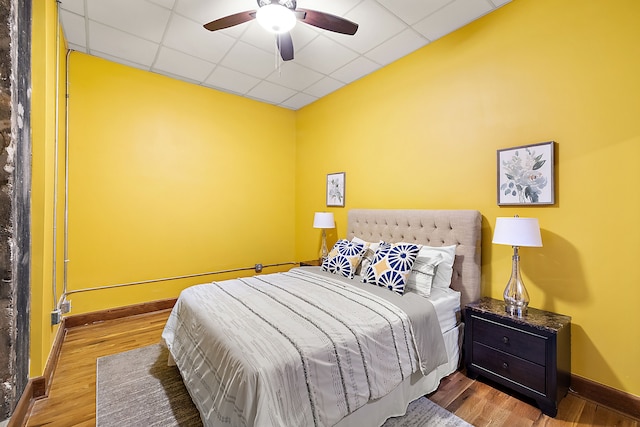 bedroom with wood-type flooring, a drop ceiling, and ceiling fan