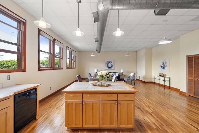 kitchen with light wood-type flooring, a paneled ceiling, decorative light fixtures, dishwasher, and tile counters