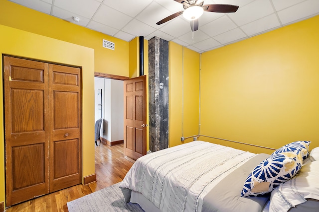 bedroom featuring ceiling fan, a closet, a drop ceiling, and light wood-type flooring