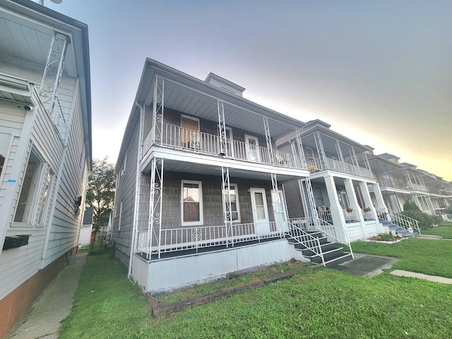 view of front of home with a porch, a balcony, and a lawn