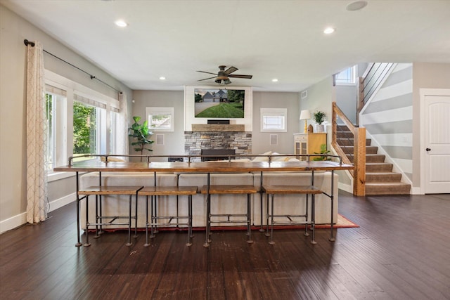 bar featuring ceiling fan, a stone fireplace, and dark wood-type flooring