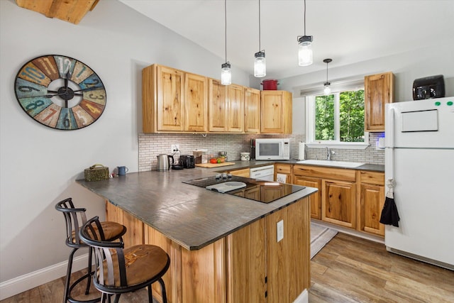 kitchen featuring kitchen peninsula, a kitchen breakfast bar, white appliances, vaulted ceiling, and sink