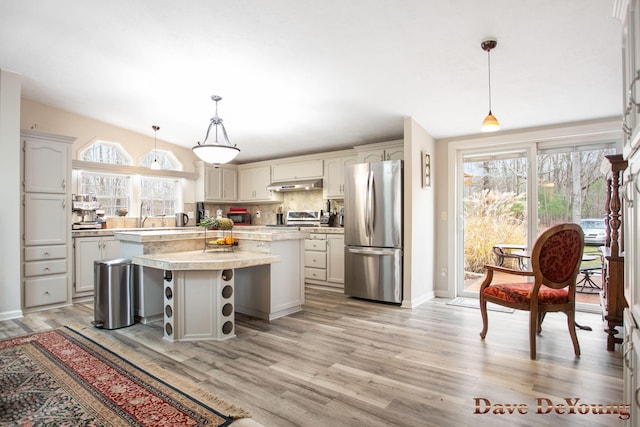 kitchen with light wood-type flooring, tasteful backsplash, stainless steel appliances, decorative light fixtures, and a kitchen island